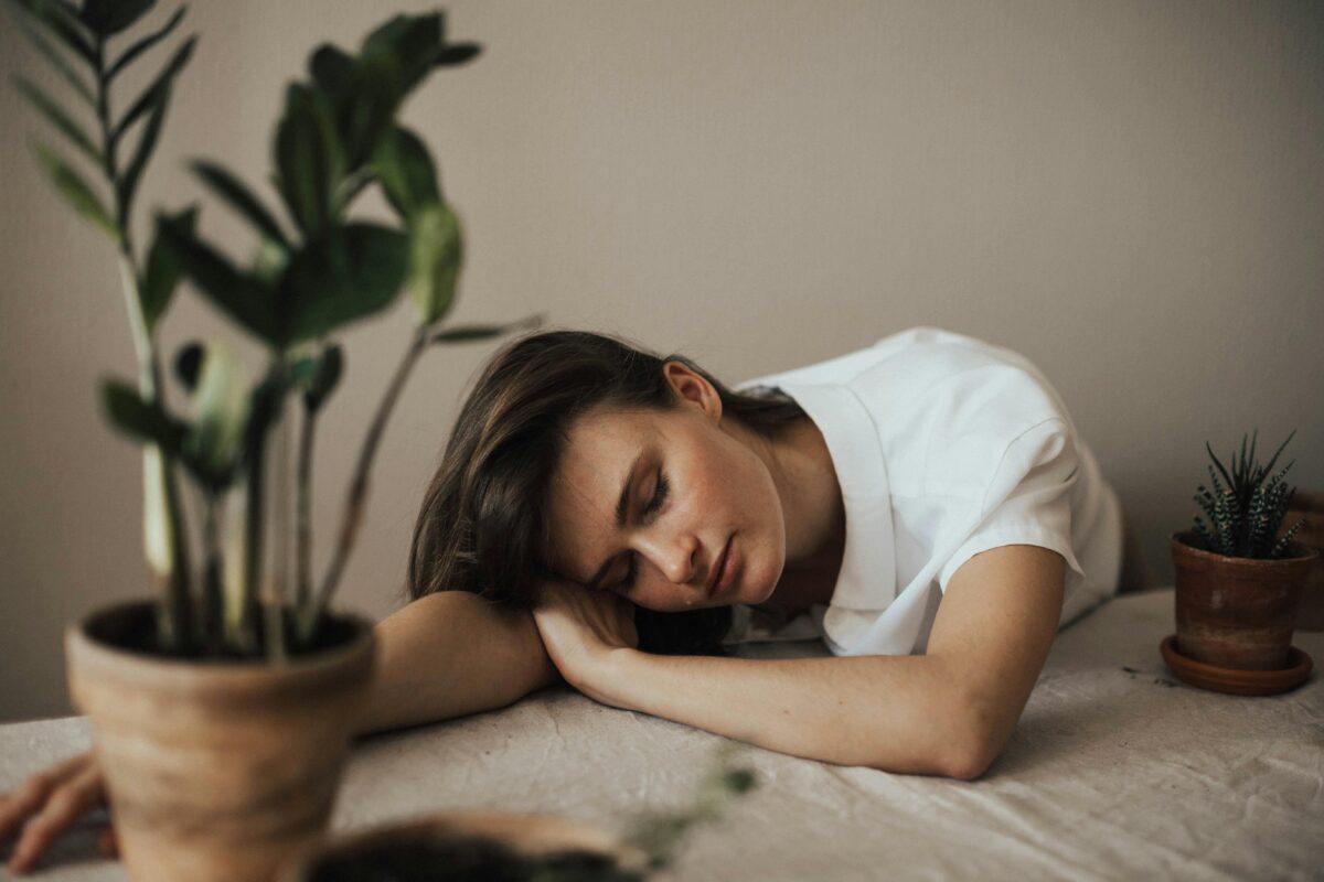 Woman is very tired, she is laying her head on a table with plants on it.