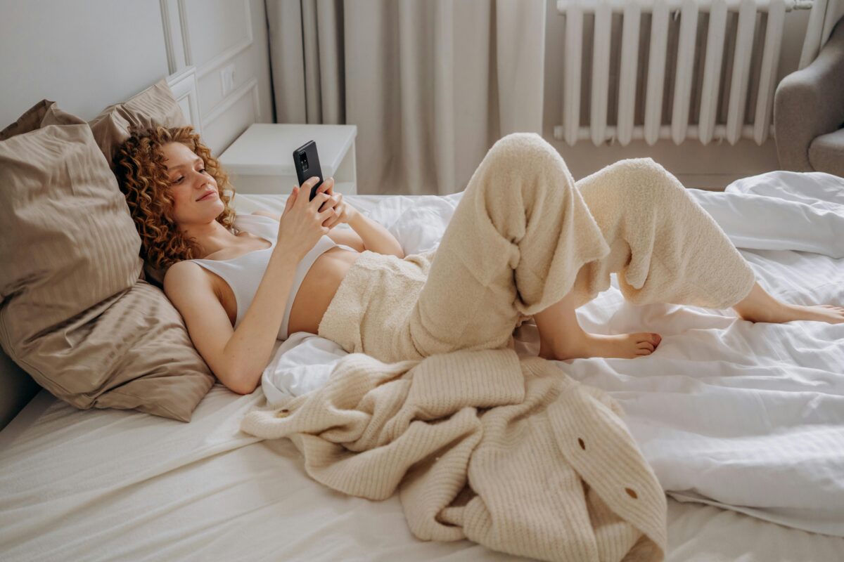 Young woman lounging in her bed while texting on her phone.