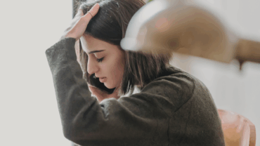 Young woman holding her head in her hand, looking stressed and tired.