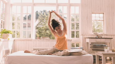 A young woman stretching in her bed while she is waking up, to get ready for the day ahead.
