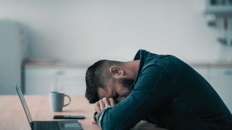 Man sitting in his kitchen, has his head down on the kitchen table stressed about his business